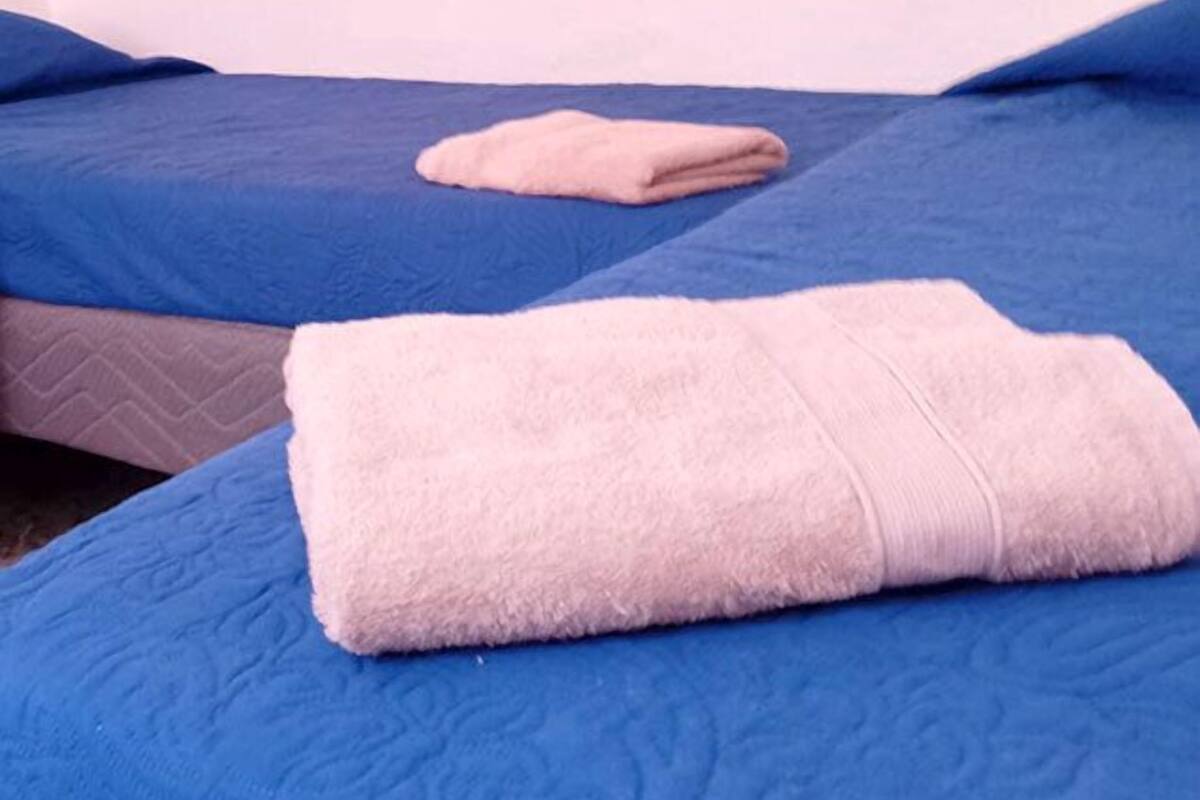 Ein Zimmer mit zwei Betten, jeweils mit blauer Bettdecke und rosa Handtuch.