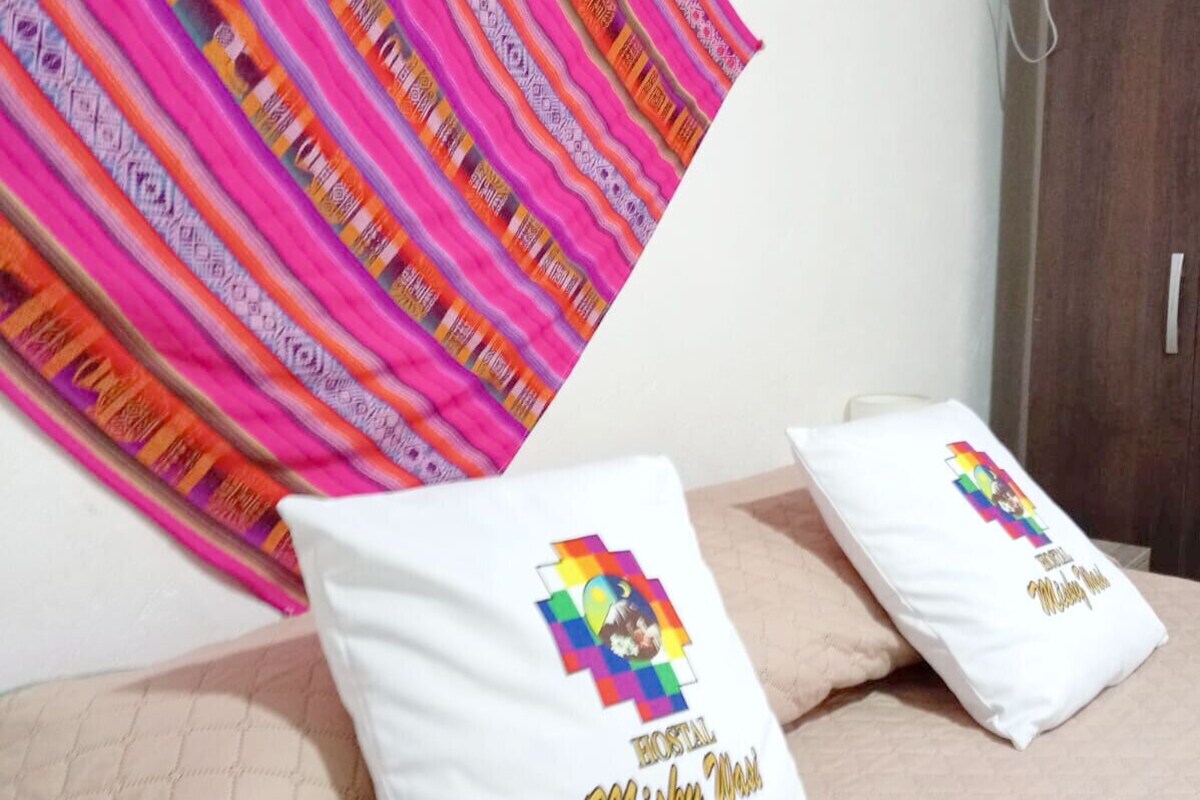 Una cama con dos almohadas, un edredón a rayas de colores y una pared blanca.