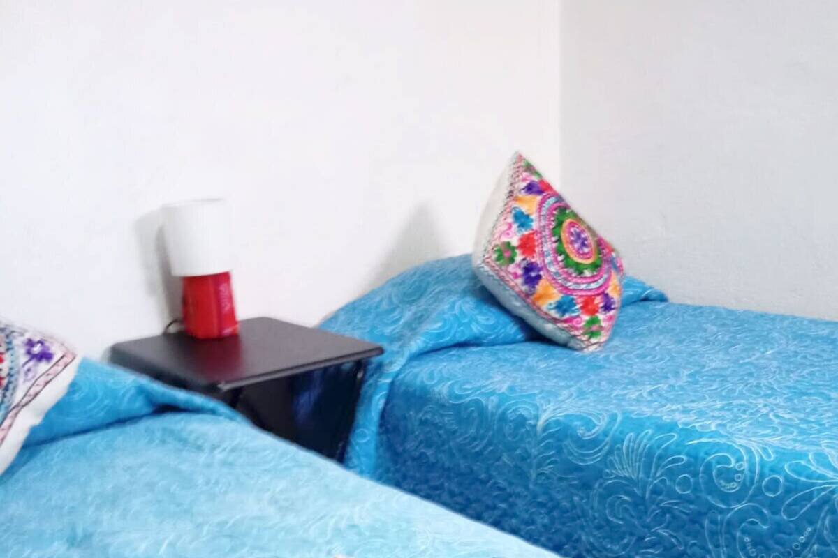 Ein Hotelzimmer mit zwei Betten, einem Nachttisch, einer roten Tasse und einem farbenfrohen Kissen.
