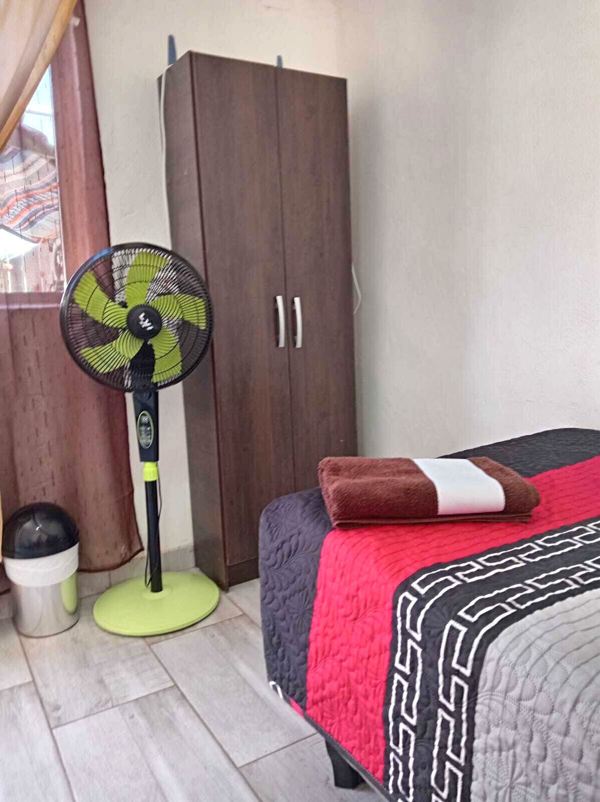 Un dormitorio con cama, ventilador, armario y ventana.