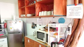 Een compacte keuken met een koelkast, magnetron en houten kastjes. Er staat een bord met een vermelding van een gemeenschappelijke ruimte voor algemeen gebruik.