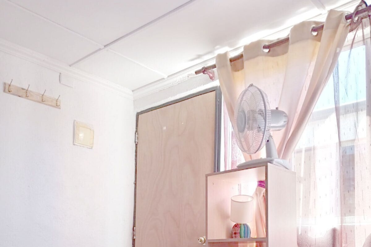 Un dormitorio con cama, mesita de noche, armario, espejo y ventana con cortinas.