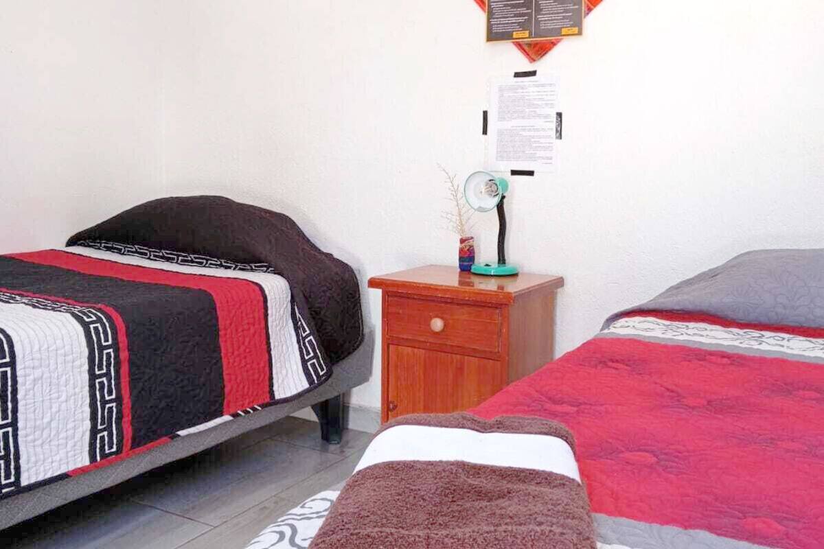 Ein Schlafzimmer mit zwei Betten, einem Nachttisch, einer Wanduhr und einem Korkbrett mit Papieren.