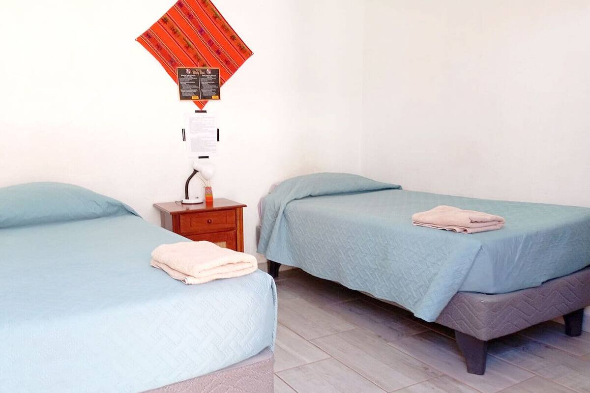 Ein Schlafzimmer mit zwei Betten, einem Nachttisch, einer Lampe und einem Gegenstand an der Wand.