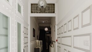 A hallway with white walls, a black carpet, and a ceiling with a decorative light fixture. - The Hyde Hotel (London)
