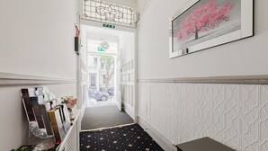 A hallway with a patterned carpet, a framed picture on the wall, and a small table. - The Hyde Hotel (London)