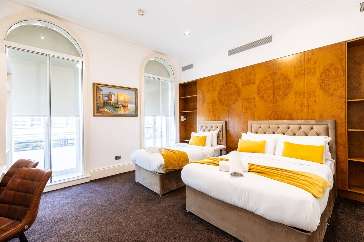 A hotel room with two beds, a large window, and a painting on the wall.