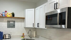 Een moderne keuken met witte kastjes, een roestvrijstalen magnetron, een waterkoker en een vaatwasser.