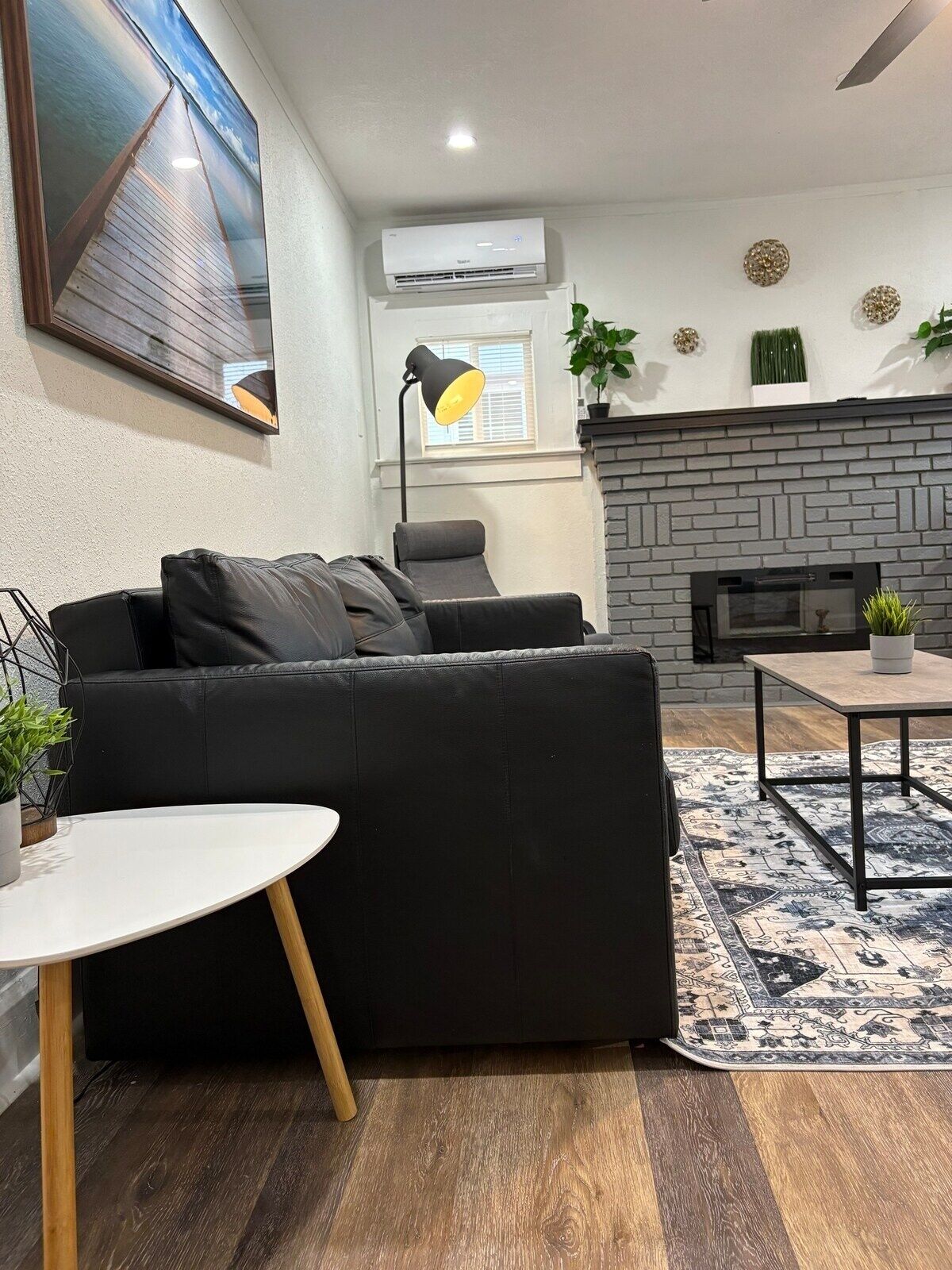 Un salon moderne avec un canapé en cuir noir, une table basse ronde blanche, une cheminée et un tapis à motifs.