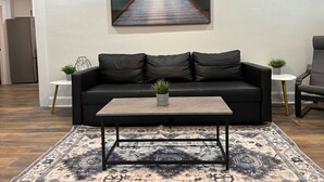 Een woonkamer met een zwarte leren bank, een bijzettafeltje en een vloerkleed.