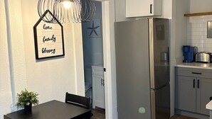 Een moderne keuken met een roestvrijstalen koelkast, witte kasten en een houten eettafel met stoelen.