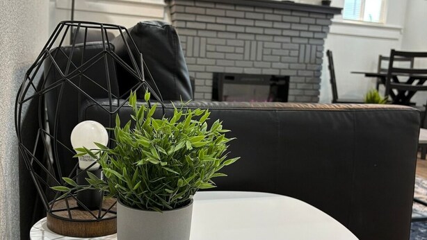 Een woonkamer met een ronde witte tafel, een zwarte bank, een vloerlamp in het zwart en een potplant.