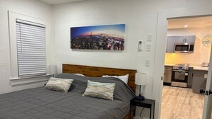 A bedroom with a bed, pillows, a nightstand, a wall clock, and a cityscape painting. - St. Pete 5th Ave Oasis (St. Petersburg)