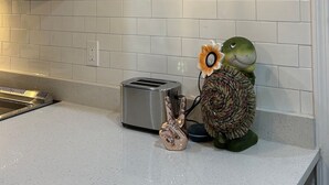 A kitchen with a round wall clock, a toaster, a decorative owl, and a hanging light fixture. - St. Pete 5th Ave Oasis (St. Petersburg)