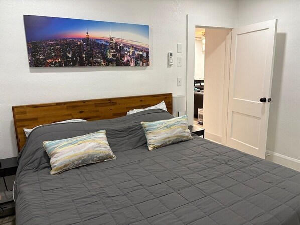A bedroom with a cityscape painting, a wooden headboard, and a gray quilted bedspread.