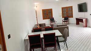 A living room with a sofa, two armchairs, a dining table with chairs, a TV, and a ceiling fan. - Melia Beach (Mbour)