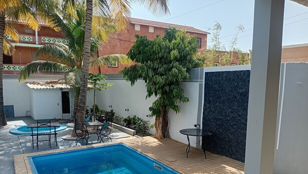 A swimming pool with a wooden deck, surrounded by potted plants and a palm tree. - Melia Beach (Mbour)