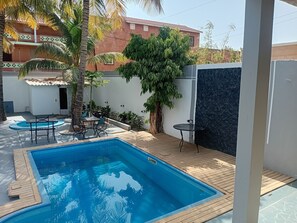A swimming pool with a wooden deck, surrounded by potted plants and a palm tree. - Melia Beach (Mbour)