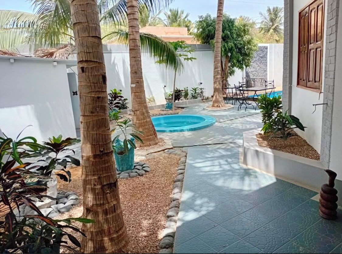 A courtyard with a swimming pool, palm trees, and a tiled walkway.