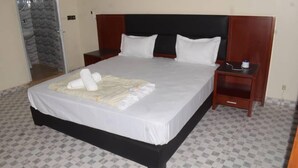 A neatly made bed with white linens, a wooden headboard, and a bedside table with a lamp. - Melia Beach (Mbour)