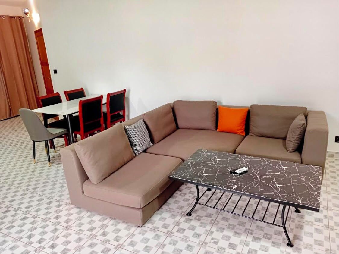 A modern living room with a sectional sofa, a dining table with chairs, and a marble coffee table.