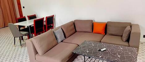 A modern living room with a sectional sofa, a dining table with chairs, and a marble coffee table.