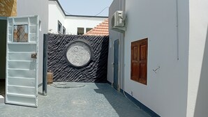 A narrow alleyway with a decorative wall, a metal gate, and a small circular window. - Melia Beach (Mbour)
