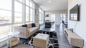 A spacious living area with large windows, a sofa, a coffee table, and a TV mounted on the wall.