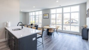 A modern kitchen with a large island, a dining area with a round table, and large windows offering a view of the outside.