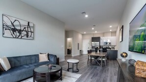 A modern living room with a blue sofa, a round coffee table, and a dining area with a wooden table and chairs.