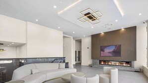 A modern living room with a curved white sofa, a flat-screen TV mounted above a fireplace, and recessed ceiling lighting.
