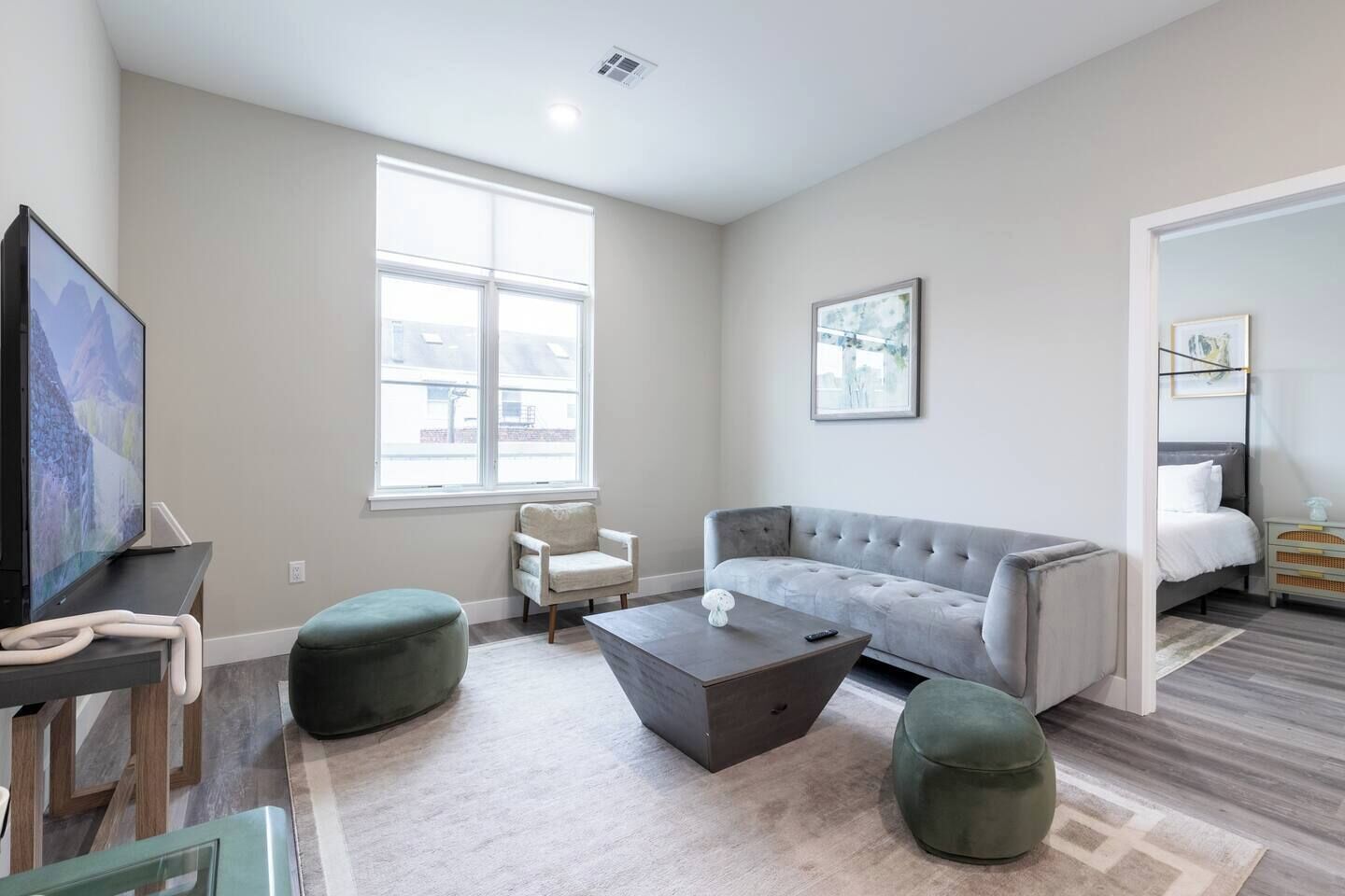 Un salon moderne avec un canapé gris, une table basse et un téléviseur. Une fenêtre laisse entrer la lumière naturelle et une porte donne accès à une autre pièce.