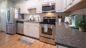 Una cocina con armarios blancos, electrodomésticos de acero inoxidable, encimera de granito y suelo de madera.