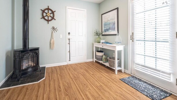 Una habitación con estufa de leña, una puerta blanca, una mesita consola con objetos decorativos y un ventanal con persianas.