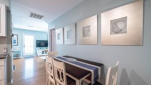 Un comedor con una mesa y sillas de madera, una cocina al fondo y obras de arte enmarcadas en la pared.