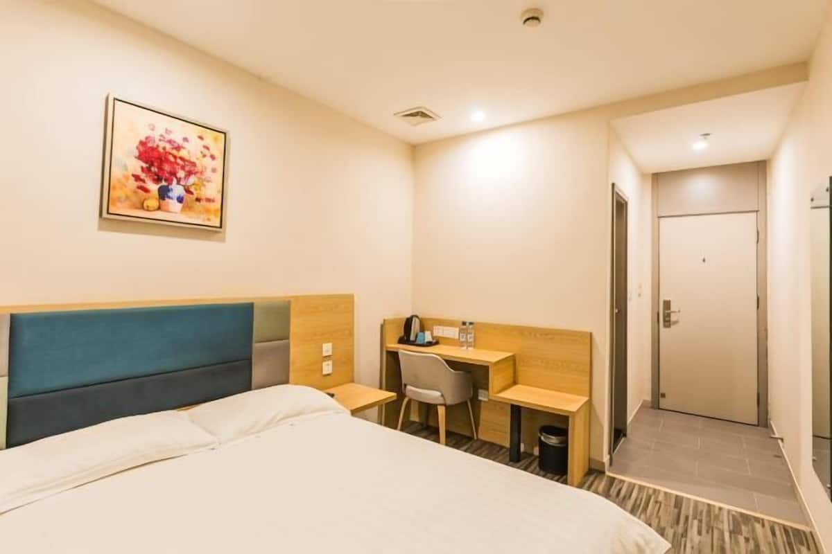 A hotel room with a bed, a desk, a chair, and a door.