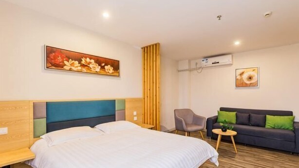 A hotel room with a bed, a sofa, a chair, and a small table. There is a painting on the wall and an air conditioning unit. - Ripple Hotel (Shanghai Xinqiao Town) (Shanghai)