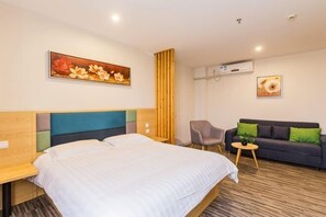 Habitación de hotel con una cama, un sofá, una silla y una mesita pequeña. Hay un cuadro en la pared y un equipo de aire acondicionado.