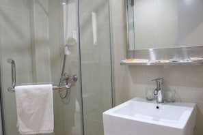 A glass-enclosed shower with a towel rack, a white sink with a mirror above, and a shelf with toiletries. - Ripple Hotel (Shanghai Xinqiao Town) (Shanghai)