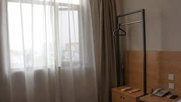 Una habitación de hotel con ventana, un armario de madera, perchero y mesita de noche con teléfono.