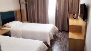 Quarto de hotel com duas camas de solteiro, uma mesa de cabeceira de madeira, televisão e cafeteira.