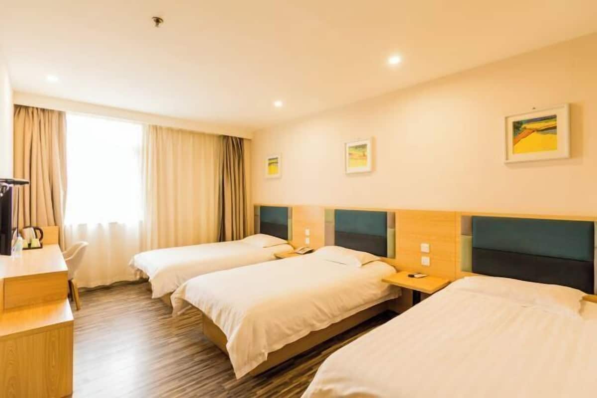 A hotel room with three beds, a desk, and a window with curtains.