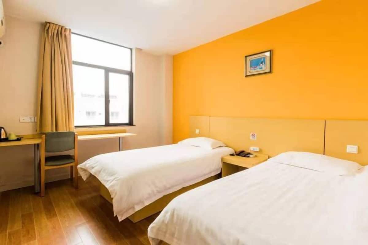 A hotel room with two beds, a desk, a chair, a window with curtains, and a picture on the wall.