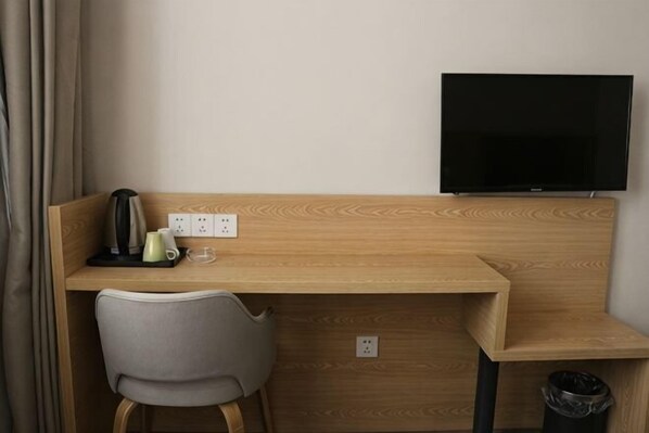 Una habitación de hotel con un escritorio de madera, un televisor, una silla y un cesto de basura.