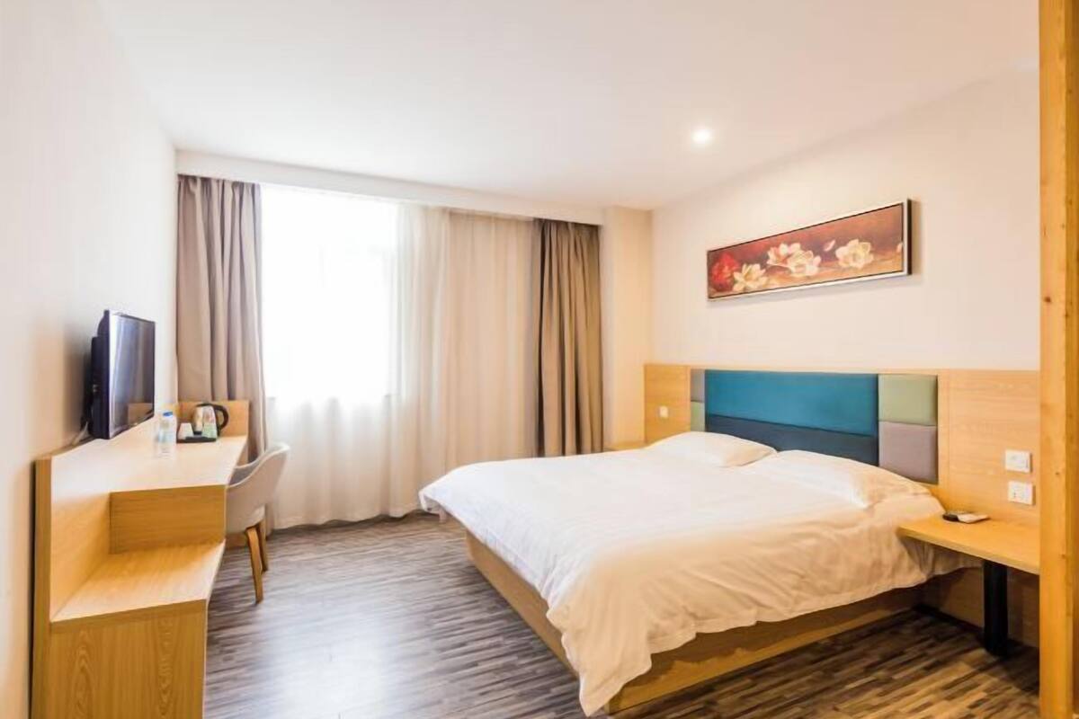 A hotel room with a bed, a desk, a chair, a TV, and a window with curtains.