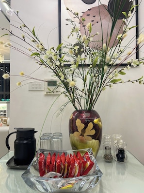 A table with a vase of flowers, a black kettle, and a bowl of snacks.