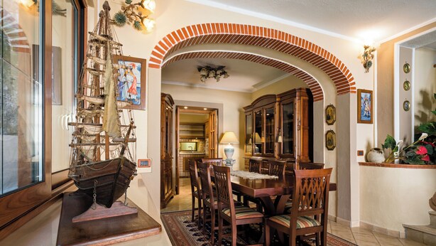 A dining area with a wooden table and chairs, a ship model, and a patterned rug. - Domus Aenaria - Spacious Villa - Prime location close to beaches and shops (Ischia)