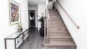 A staircase with wooden steps and a metal handrail, leading to a landing with a dark wooden floor. - Niagara Falls Area  Hidden Gem-Luxury, Cozy Canal-Side Home, Niagara Area's Hidden Gem- JNShortstay (Welland)