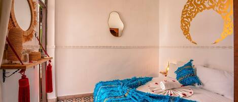 A bedroom with a bed, a wall-mounted mirror, a decorative wall piece, and a patterned floor.