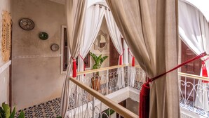 Uma varanda com grades de ferro forjado, cortinas brancas e vista para um interior tradicional.